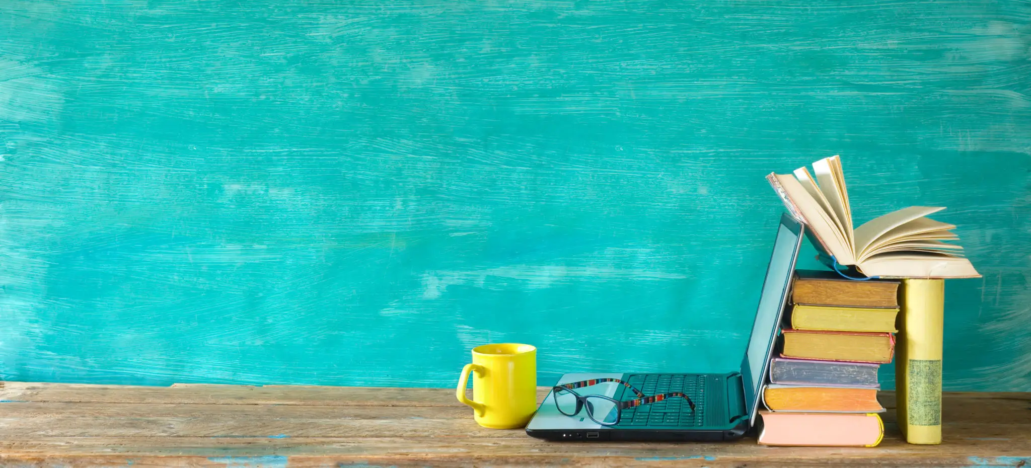 Yellow mug and closed book on wooden table against teal wall.
