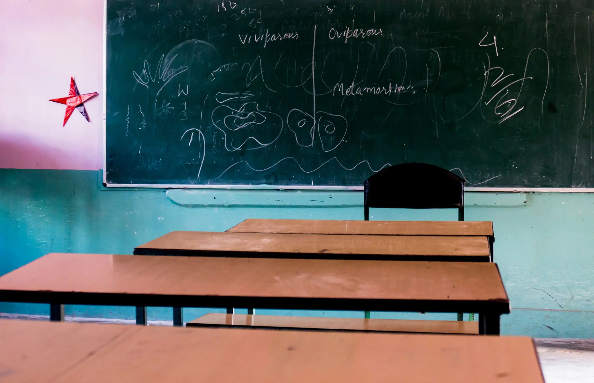 Empty classroom with wooden desks and a chalkboard displaying a diagram.