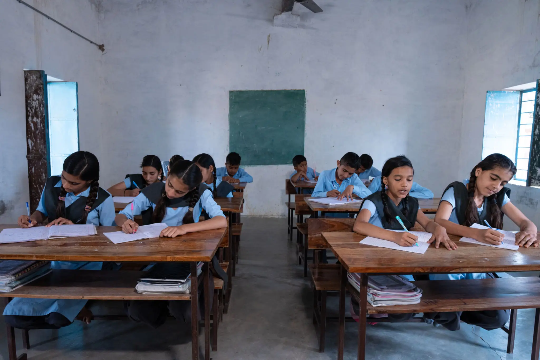 Students sitting at desks in a classroom, writing in notebooks.